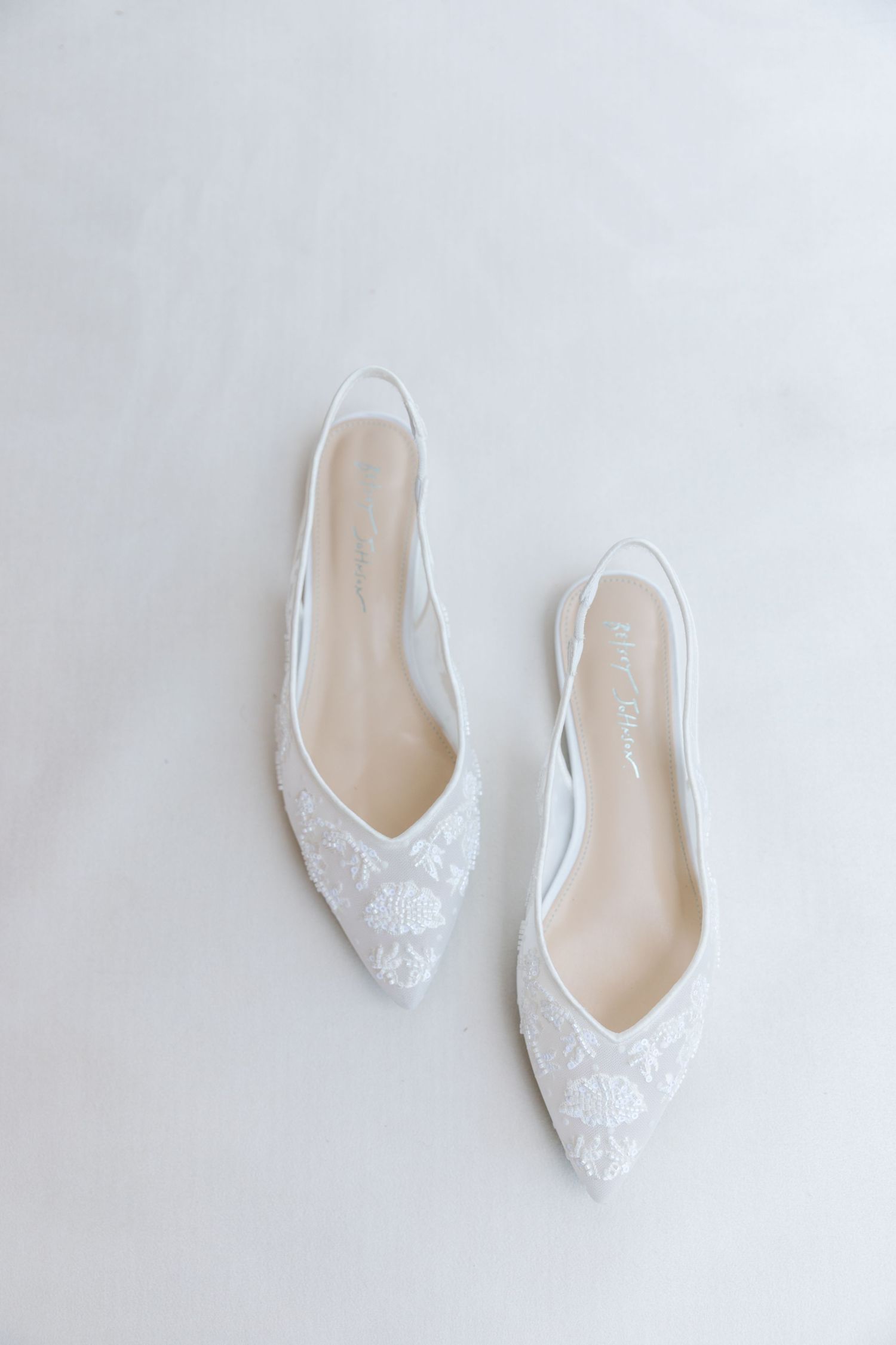 Elegant white lace bridal flats with pointed toes displayed on light background.