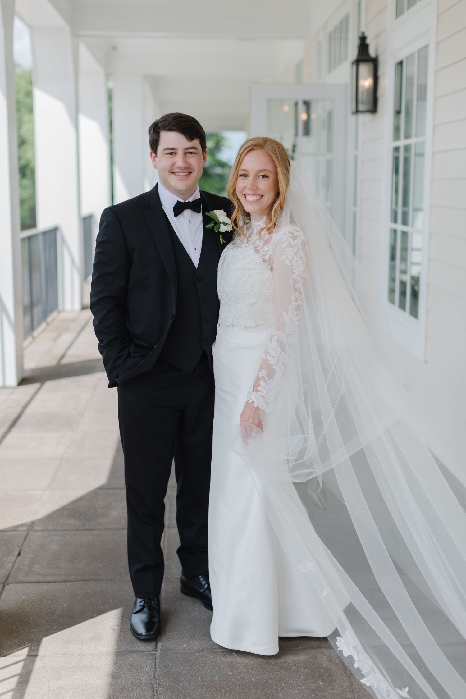 Bride and groom share joyful moments together in a bright white covered porch walkway.