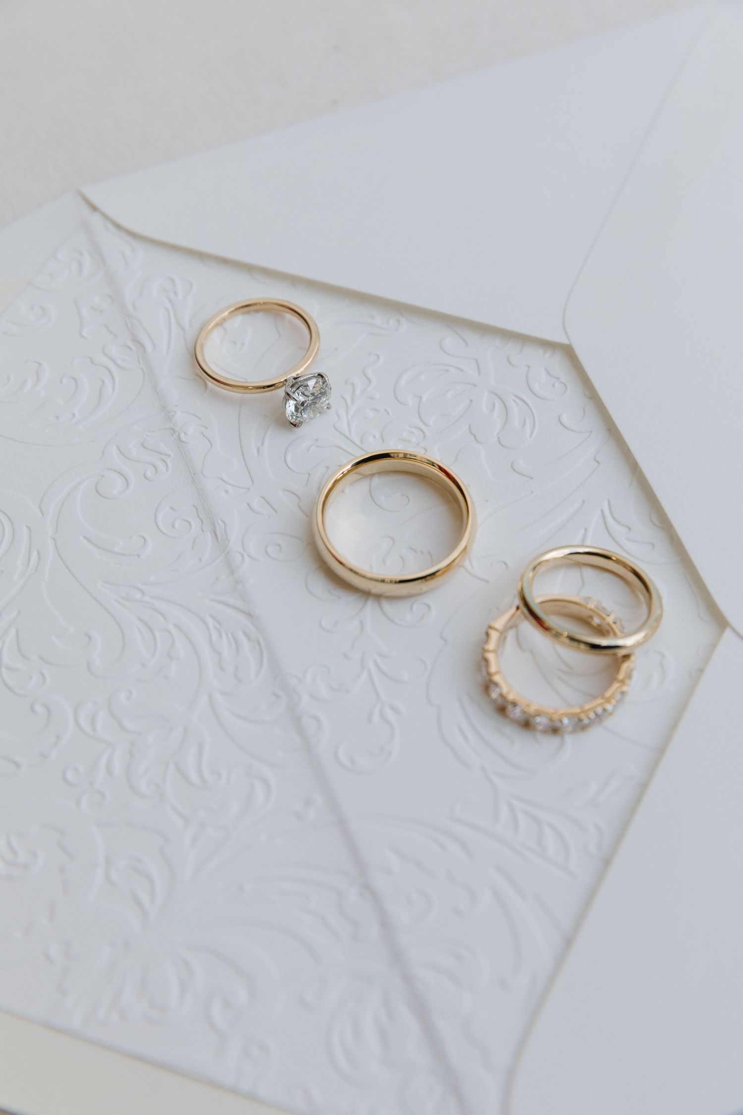 Four gold rings including an engagement ring with diamonds displayed on white embossed textured paper.