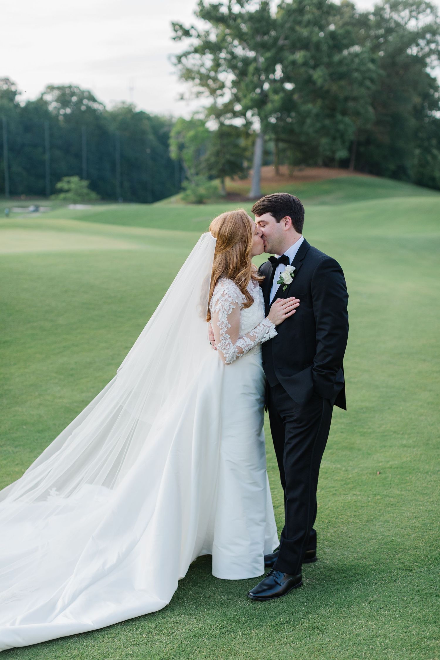 A couple in wedding attire share an intimate moment on a lush green golf course.