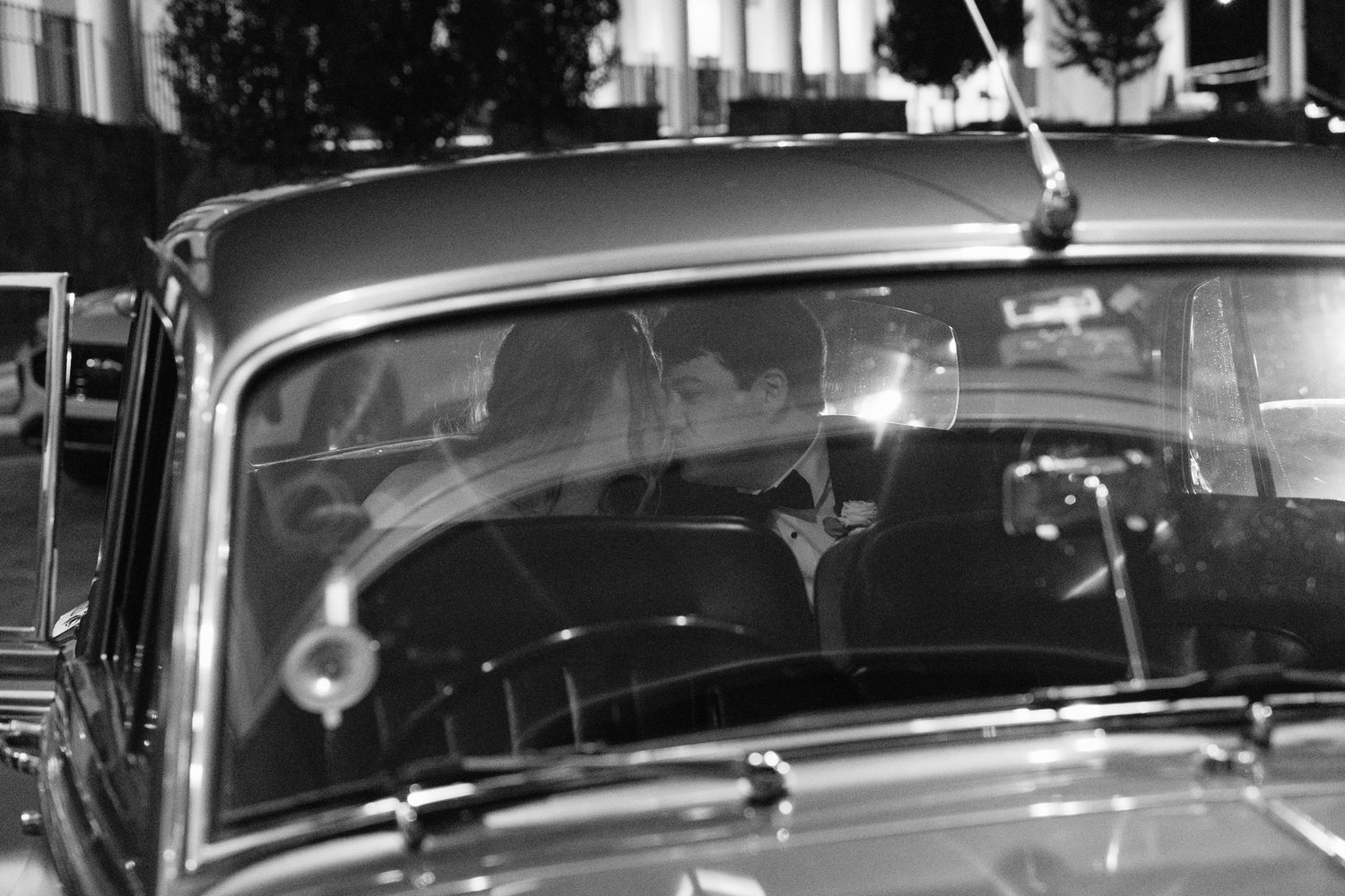 Vintage black and white photograph of a classic car driving down a city street at night.