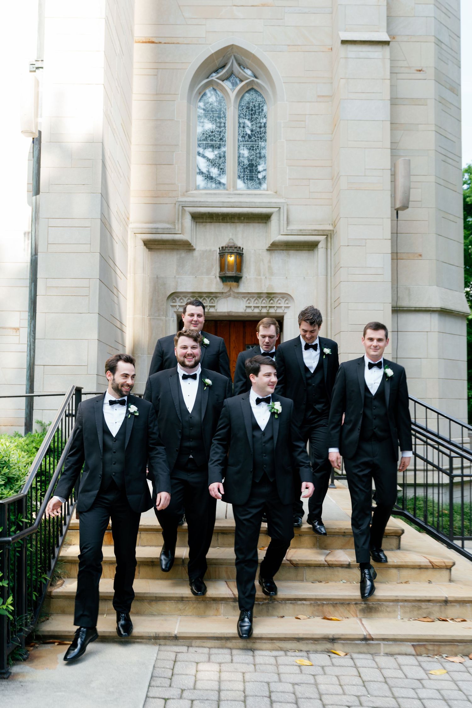 A group of groomsmen in black tuxedos walk down high-end church steps in a candid wedding photo sequence. christ the king