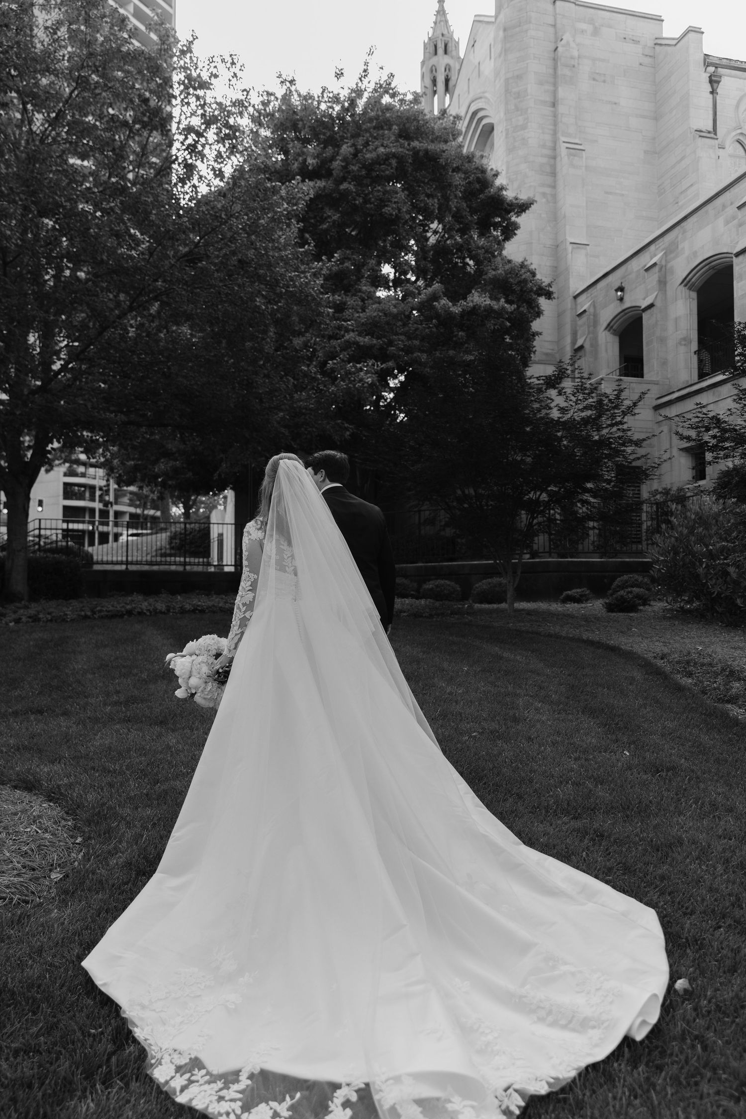 A flowing white wedding dress with a dramatic cathedral-length train photographed in a series against a church backdrop.