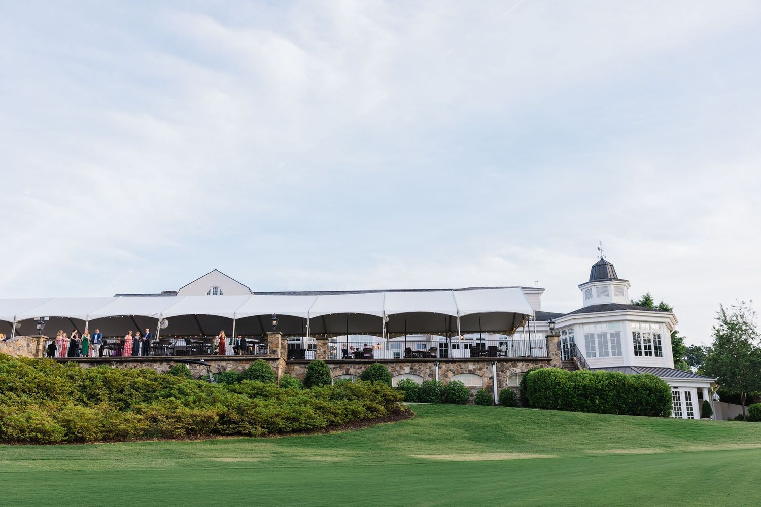 White clubhouse with covered outdoor patio overlooking a lush green golf course under blue sky.