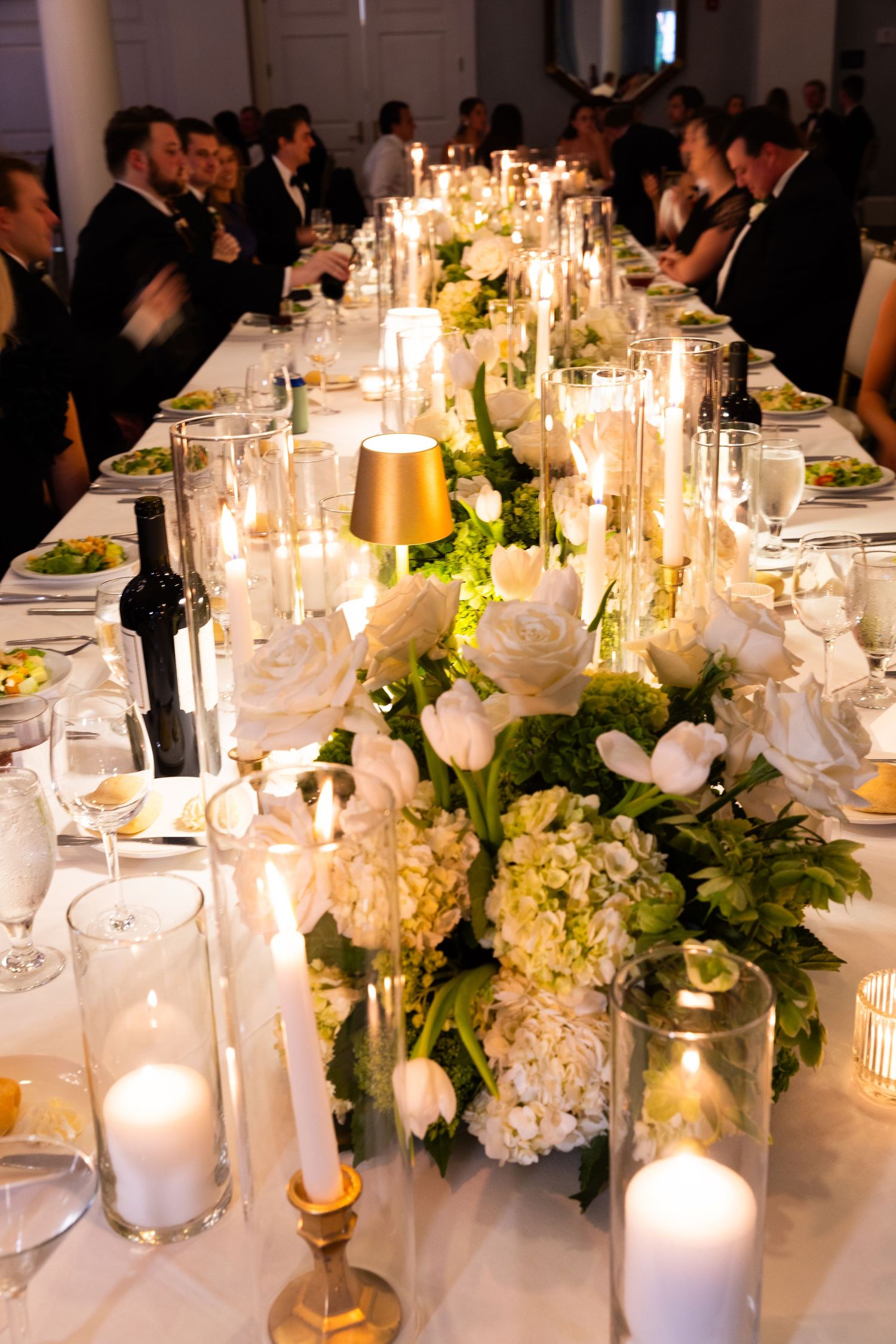 Elegant wedding reception table decorated with white floral centerpieces, glowing candles and crystal glassware.