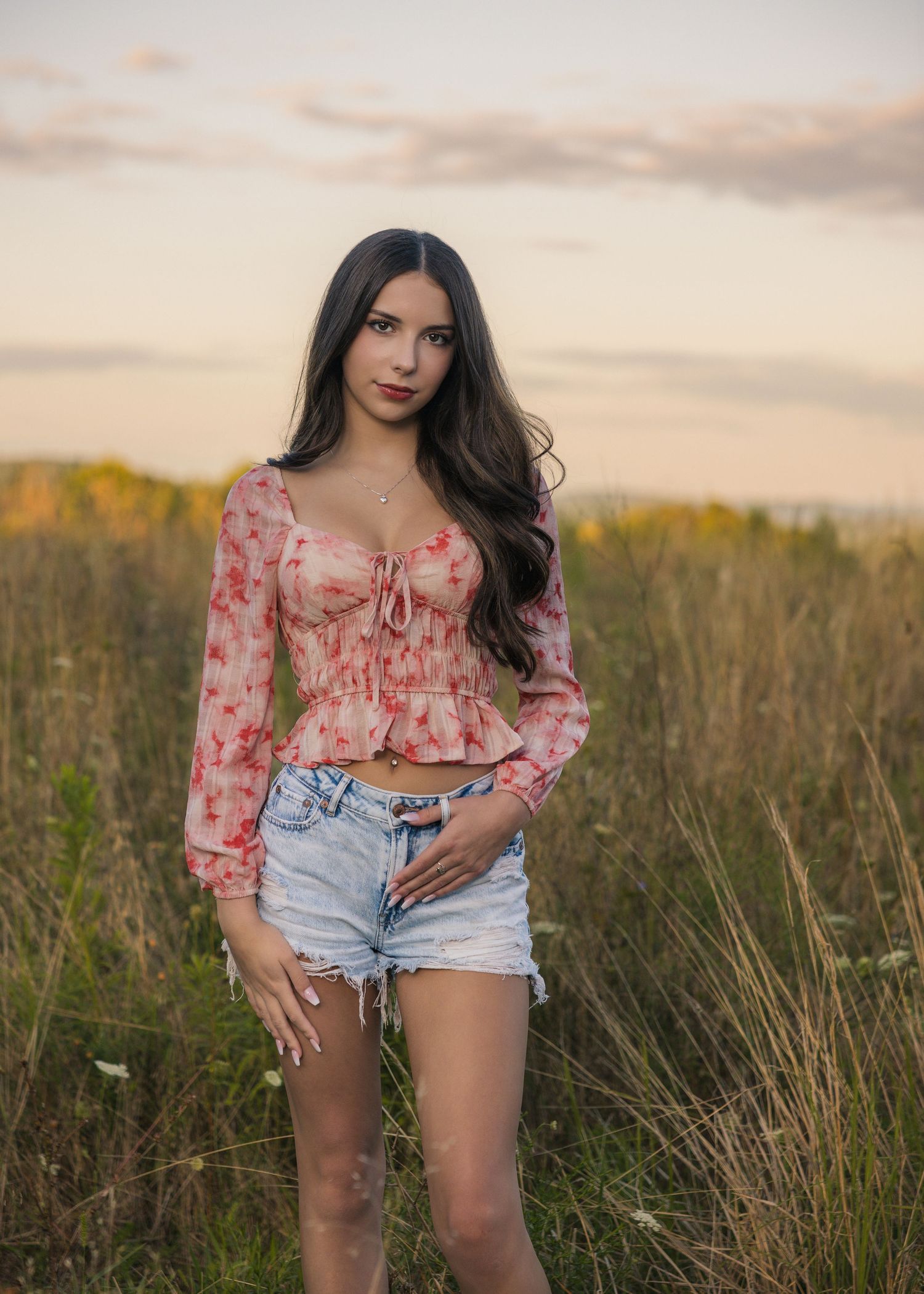 Fashion photography series in a field at sunset featuring floral top and denim shorts outfit.
