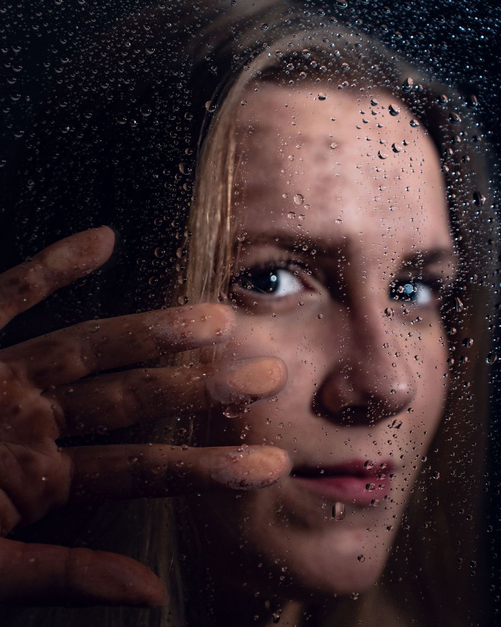 Portrait artistique à travers une vitre recouverte de pluie, avec un éclairage et des ombres spectaculaires. Florent Vause
