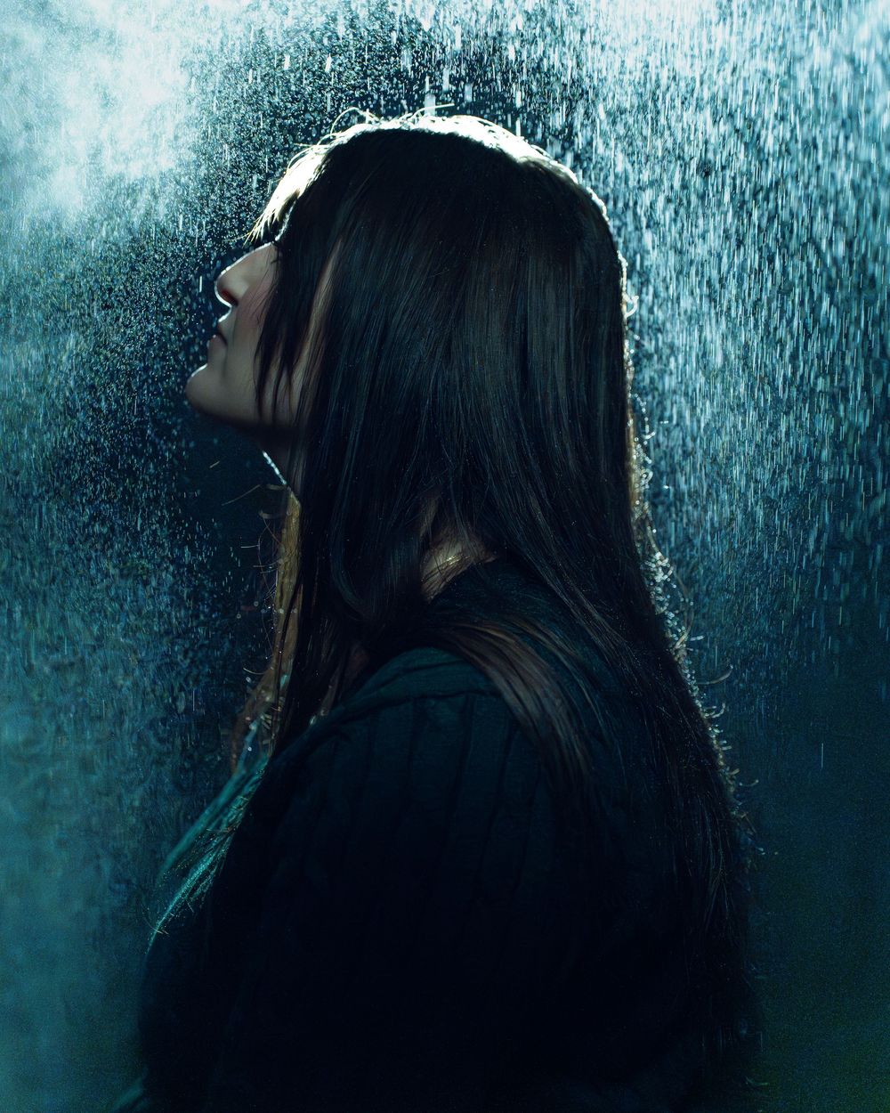 Une silhouette aux longs cheveux noirs sur fond de pluie battante et d'éclairage bleu. Florent Vause