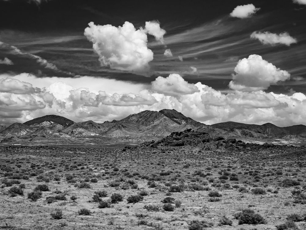 Black and white desert landscape with mountains and dramatic clouds in the sky.
