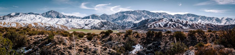 Panoramic view of snow-dusted desert mountain range under blue sky.
