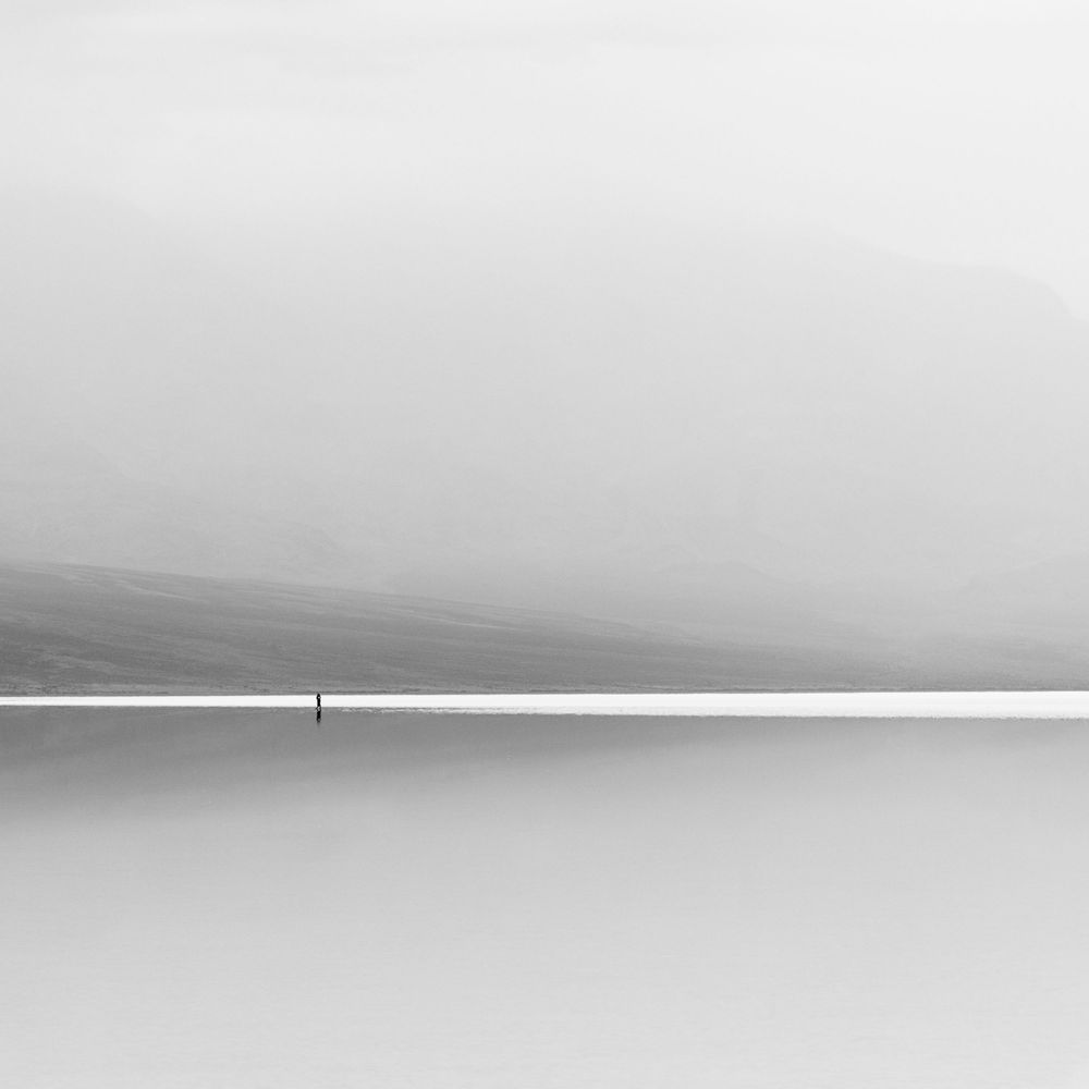 Minimalist black and white image of lone figure on misty flat horizon.