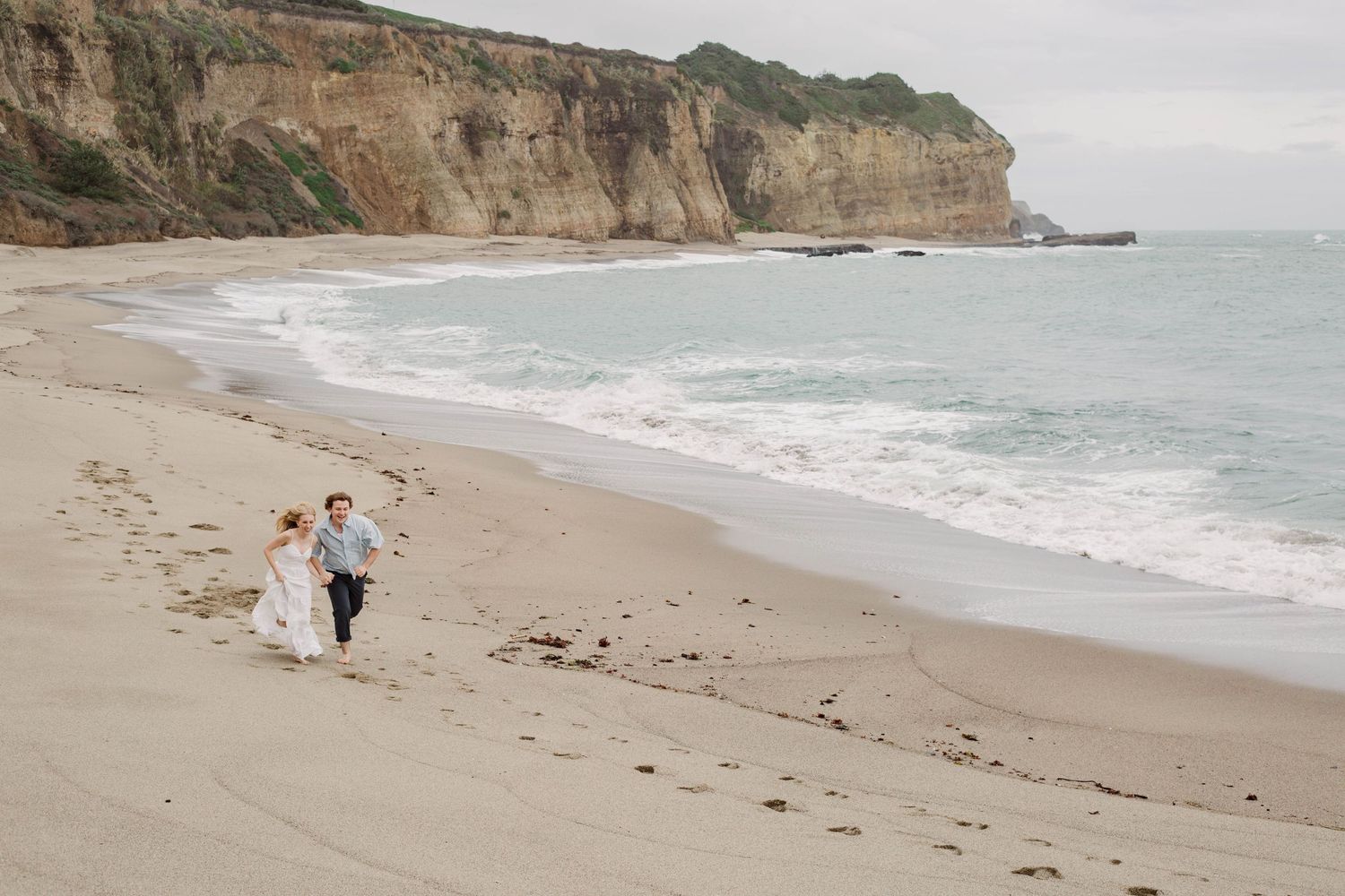 Coastal beach landscape with rocky cliffs and gentle waves rolling onto sandy shore.