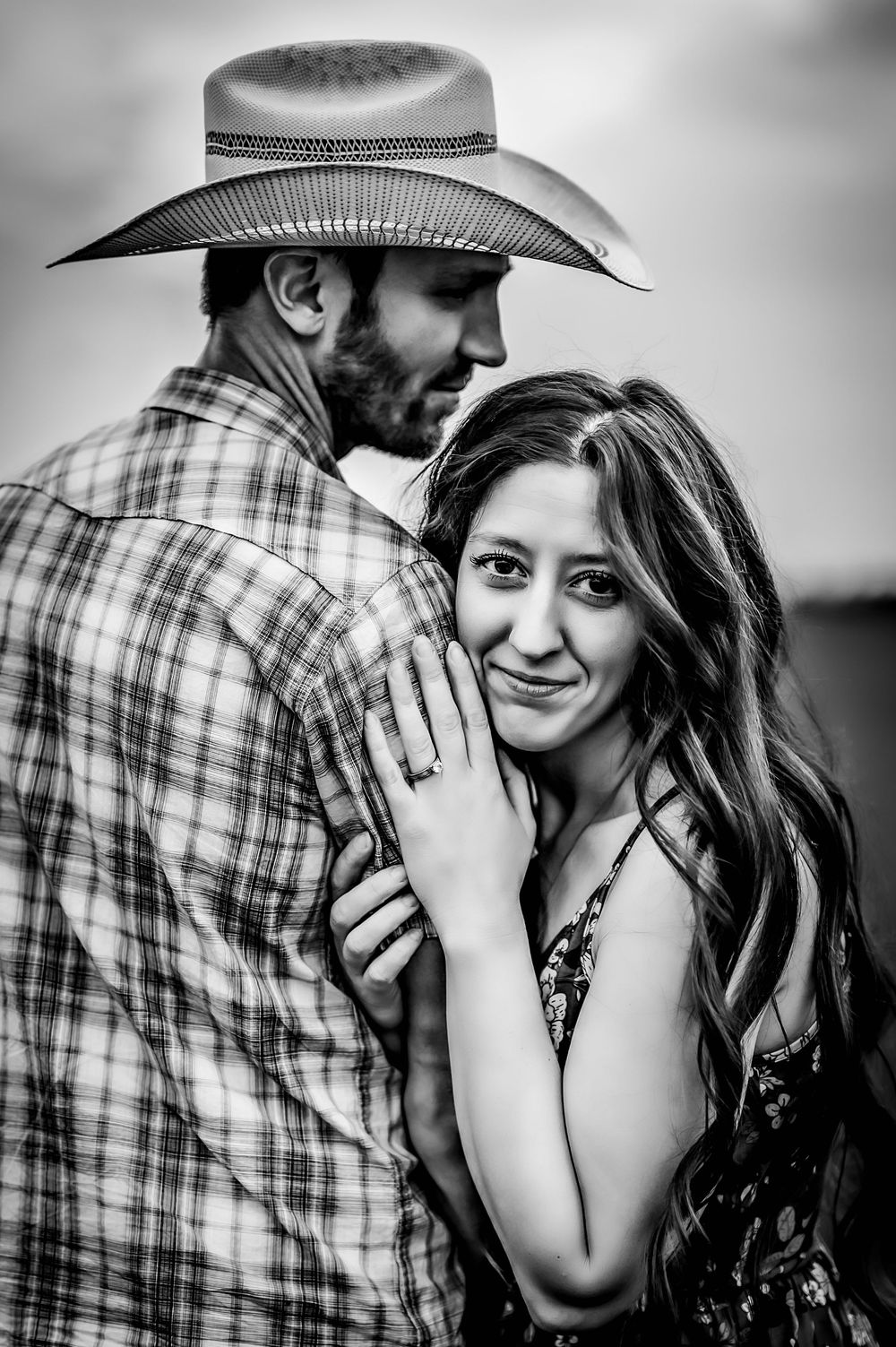 A black and white portrait of a couple in a romantic embrace with the person in plaid wearing a cowboy hat.