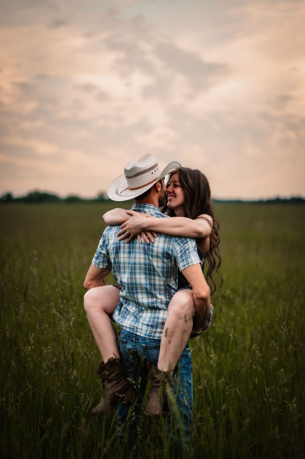 A romantic couple embracing in a green meadow field at sunset wearing coordinating plaid outfits.