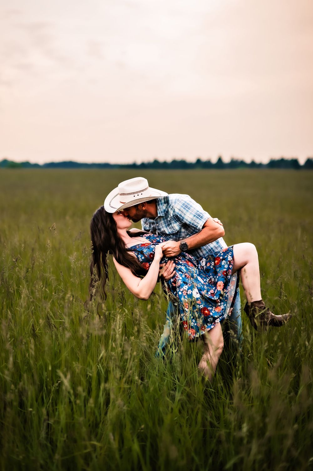 A couple dances intimately in a lush green meadow with a romantic dip pose at sunset.
