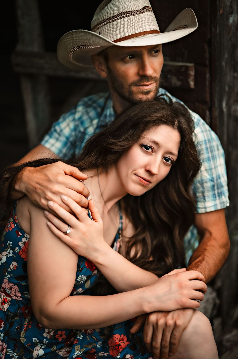 A romantic country western couple embraces in a rustic setting, wearing a floral dress and cowboy attire.