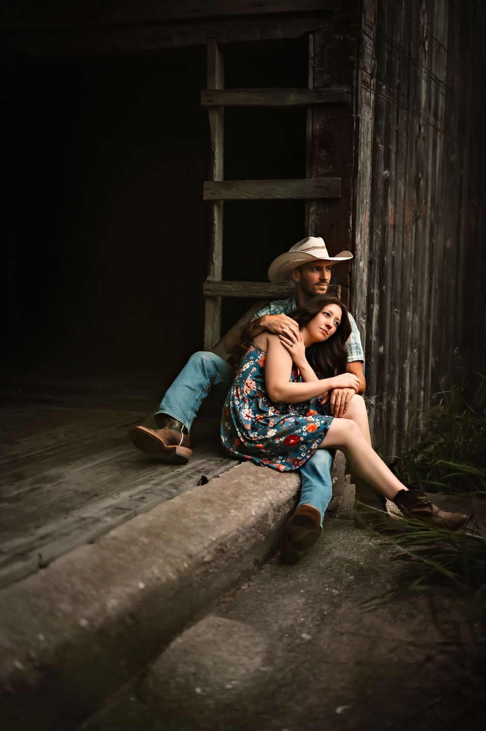 A couple shares an intimate moment on a wooden ledge in a rustic barn setting.