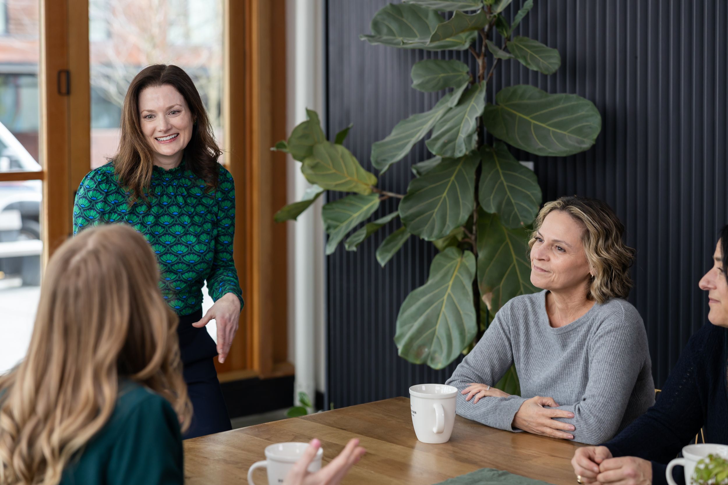 woman business coach Seattle, WA branding sitting at conference table with group of cooperate women leaders presenting