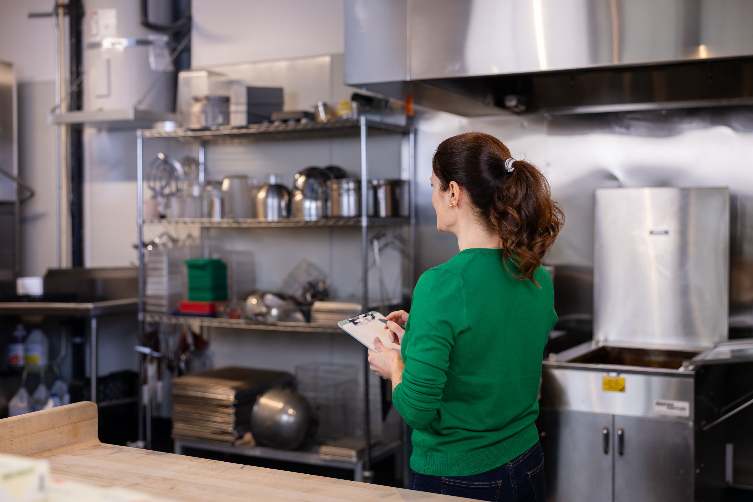 woman business coach Seattle, WA branding standing in back of kitchen of cafe taking notes about effective productive business practices