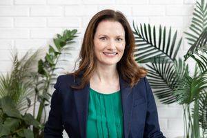 woman business coach Seattle, WA branding headshot in front of green plants and white wall smiling with green shirt & blue blazer
