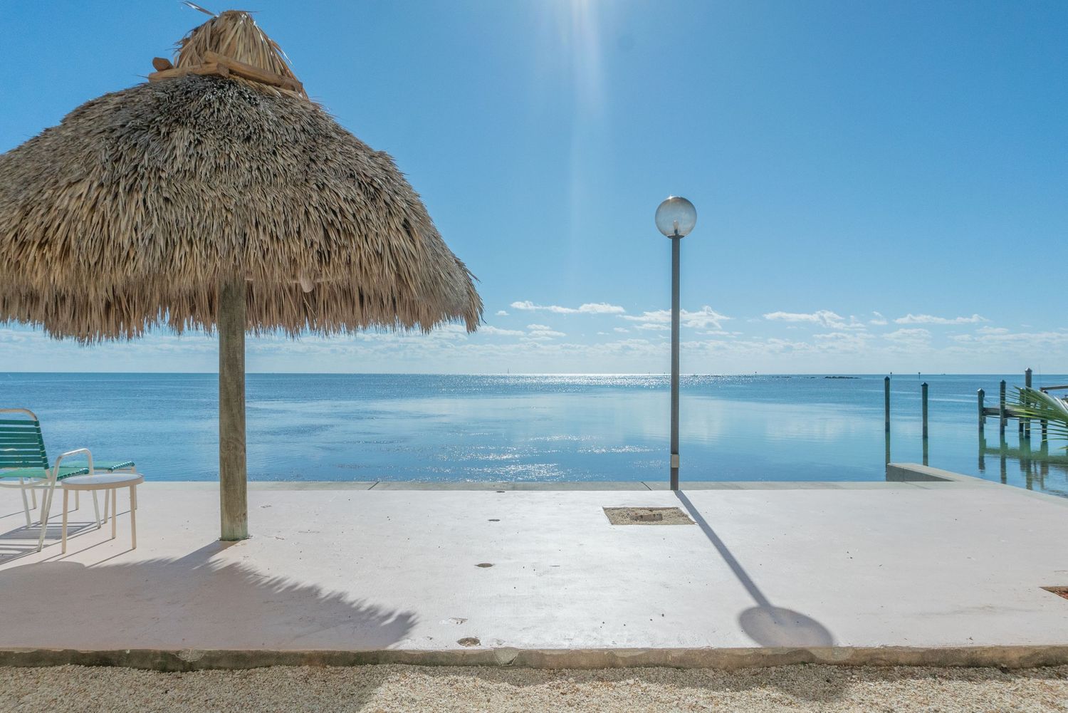 Tropical beach scene with thatched umbrella, white deck, and serene ocean view under blue sky.