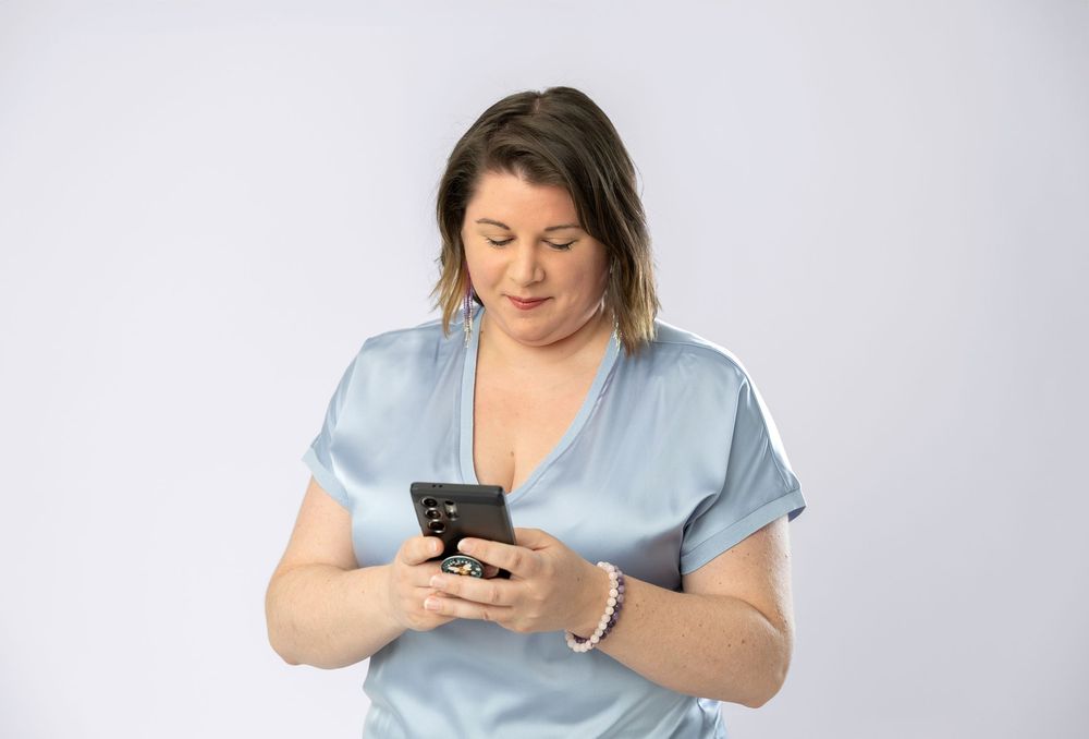 Person in light blue shirt checks phone screen while standing against plain white background.