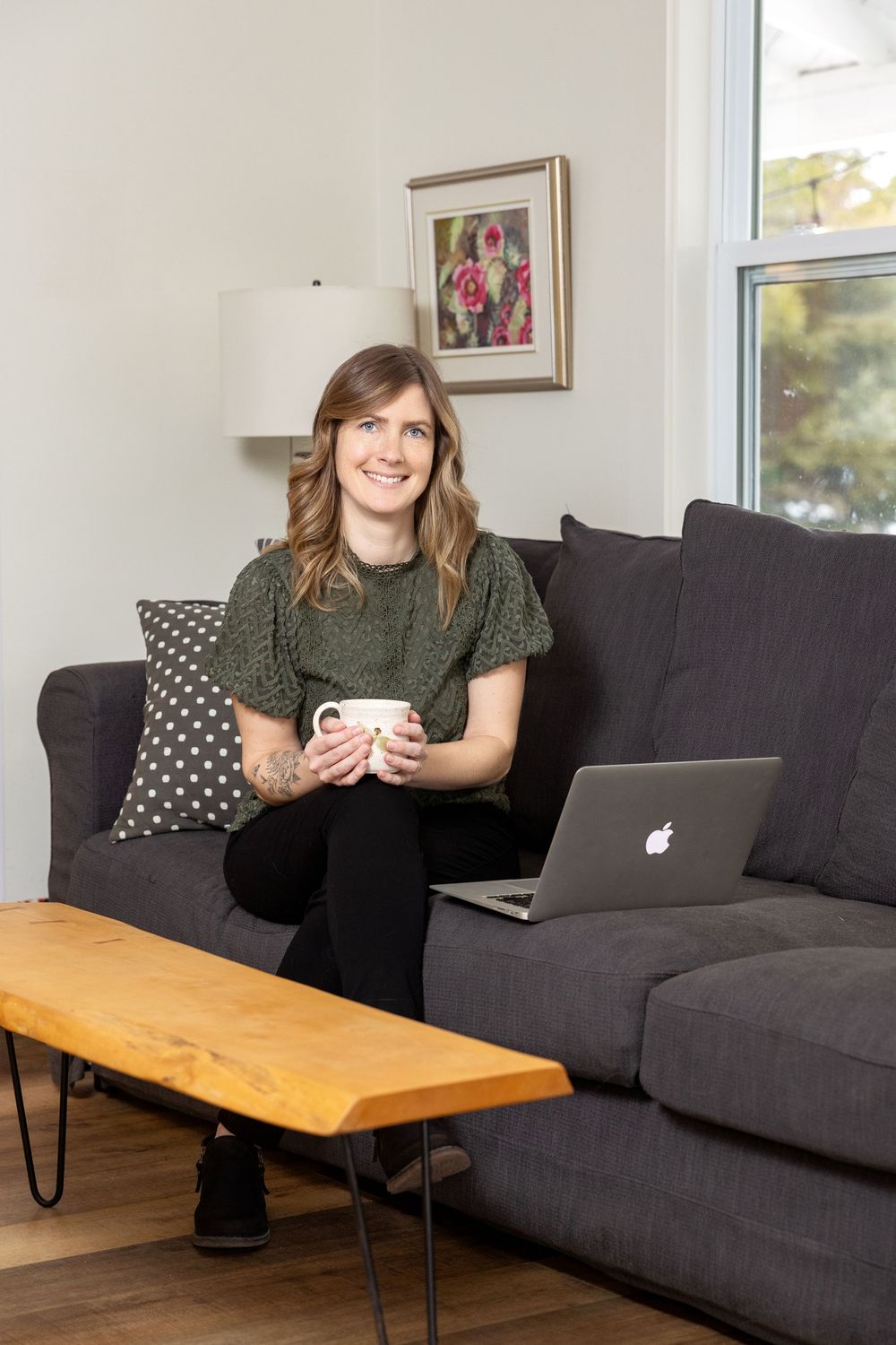 Person relaxing on a dark gray couch with laptop and coffee mug in modern living room with wooden coffee table.