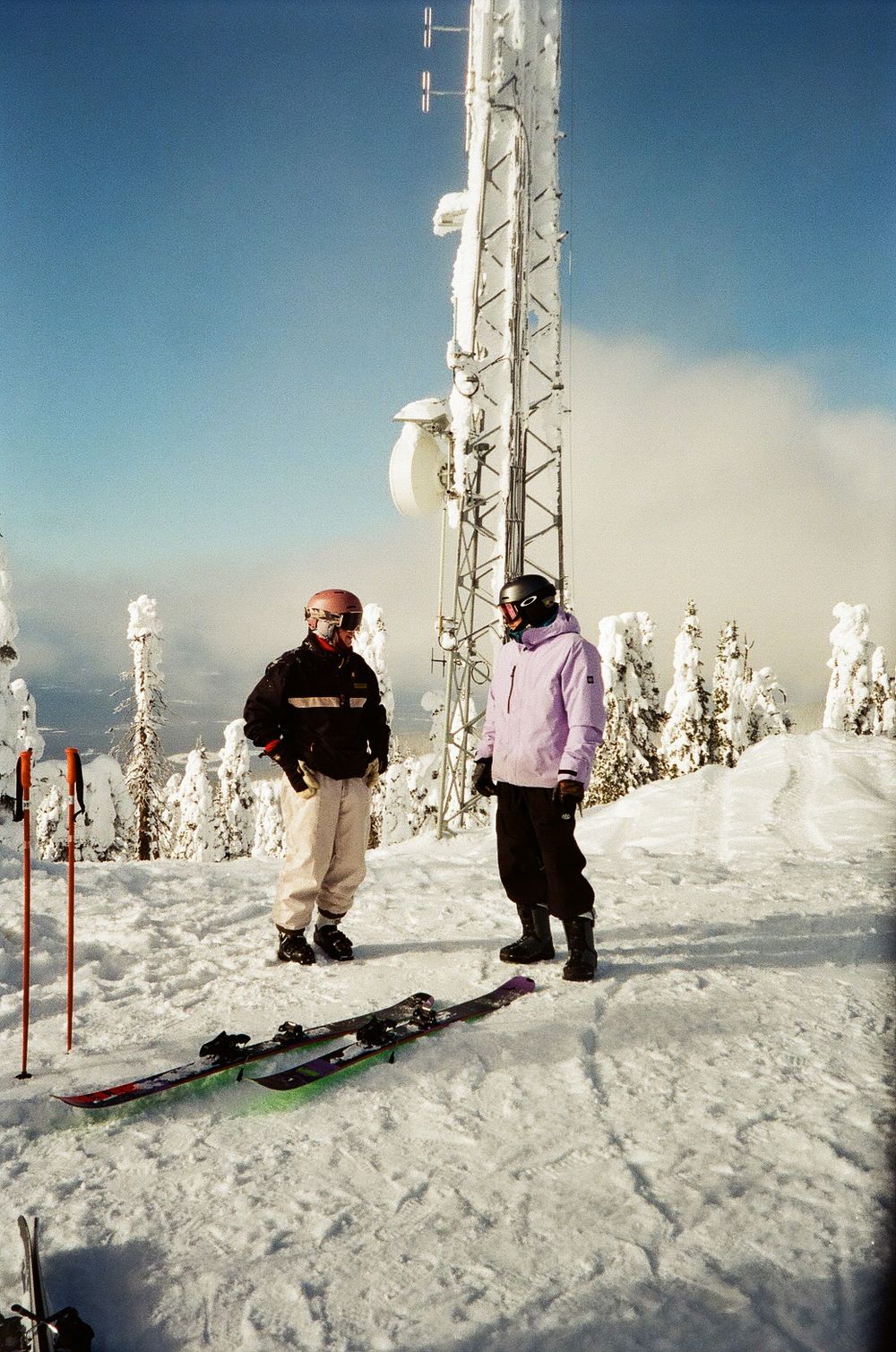 Winter sports enthusiasts prepare for skiing on a snowy mountaintop near communication towers.
