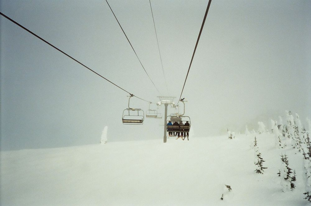 Chairlift carries skiers up a snow-covered mountain slope on a foggy winter day.