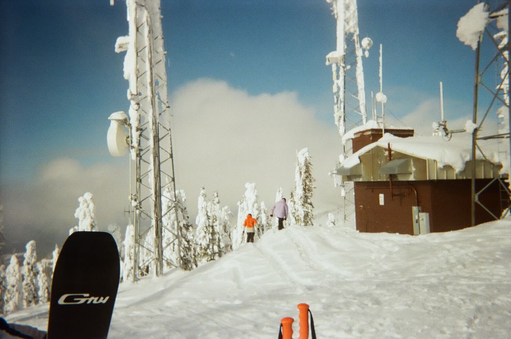 Snow-covered ski slopes with communication towers and a small building station at the summit.