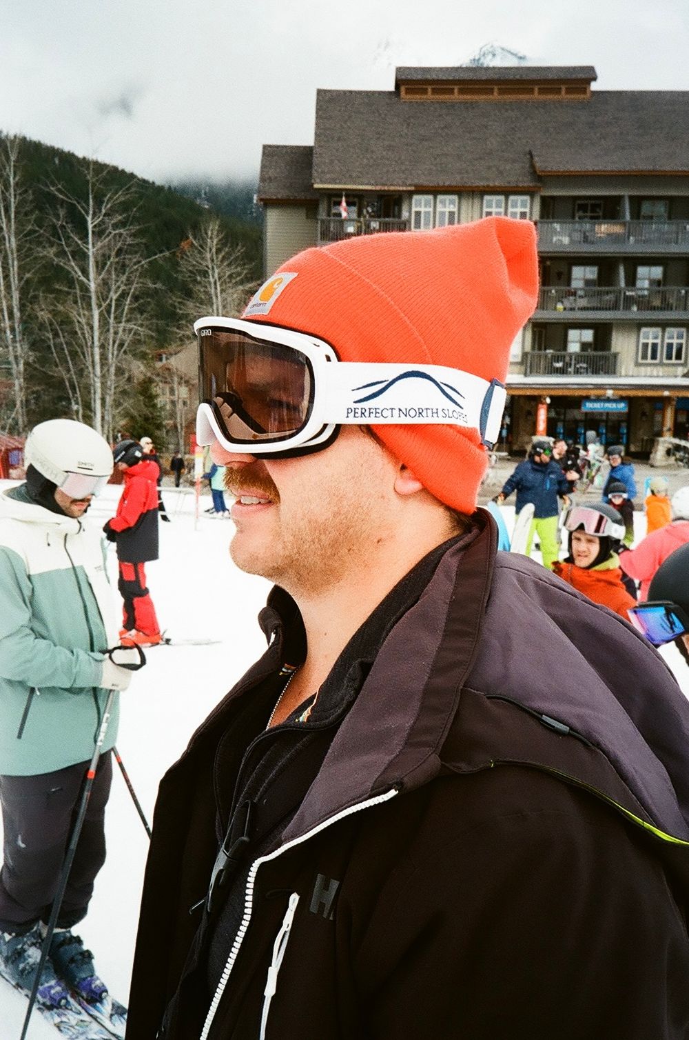 Skiers gathered at base of snowy mountain lodge wearing winter gear.