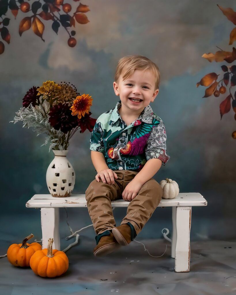 Fall themed portrait setup with a Hawaiian shirt, white bench, autumn flowers in vase, and orange pumpkins on gray backdrop.
