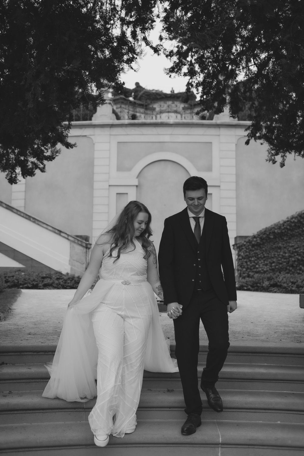 A sequence of black and white photos showing a couple walking up elegant white stone steps on their wedding day.
