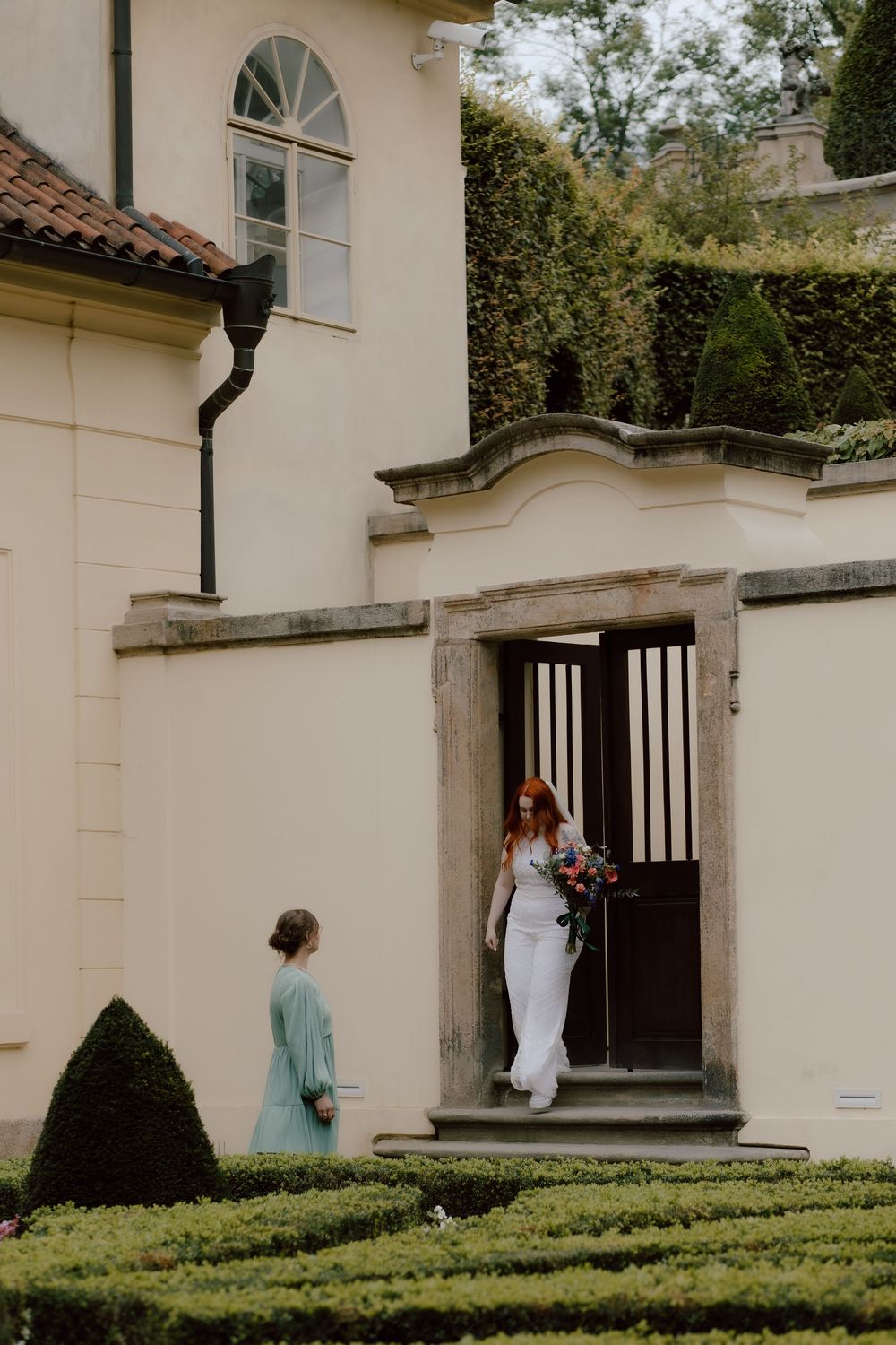An elegant wedding scene at a historic building entrance with manicured gardens and classical architecture.