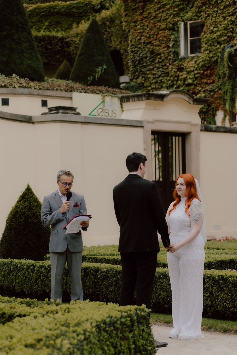 A romantic outdoor wedding ceremony in a garden with ivy-covered walls and manicured hedges.
