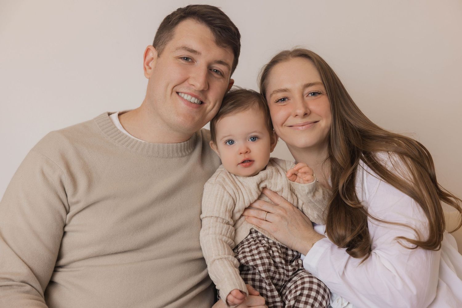 Family in coordinated beige and white outfits poses together for professional studio photographs.