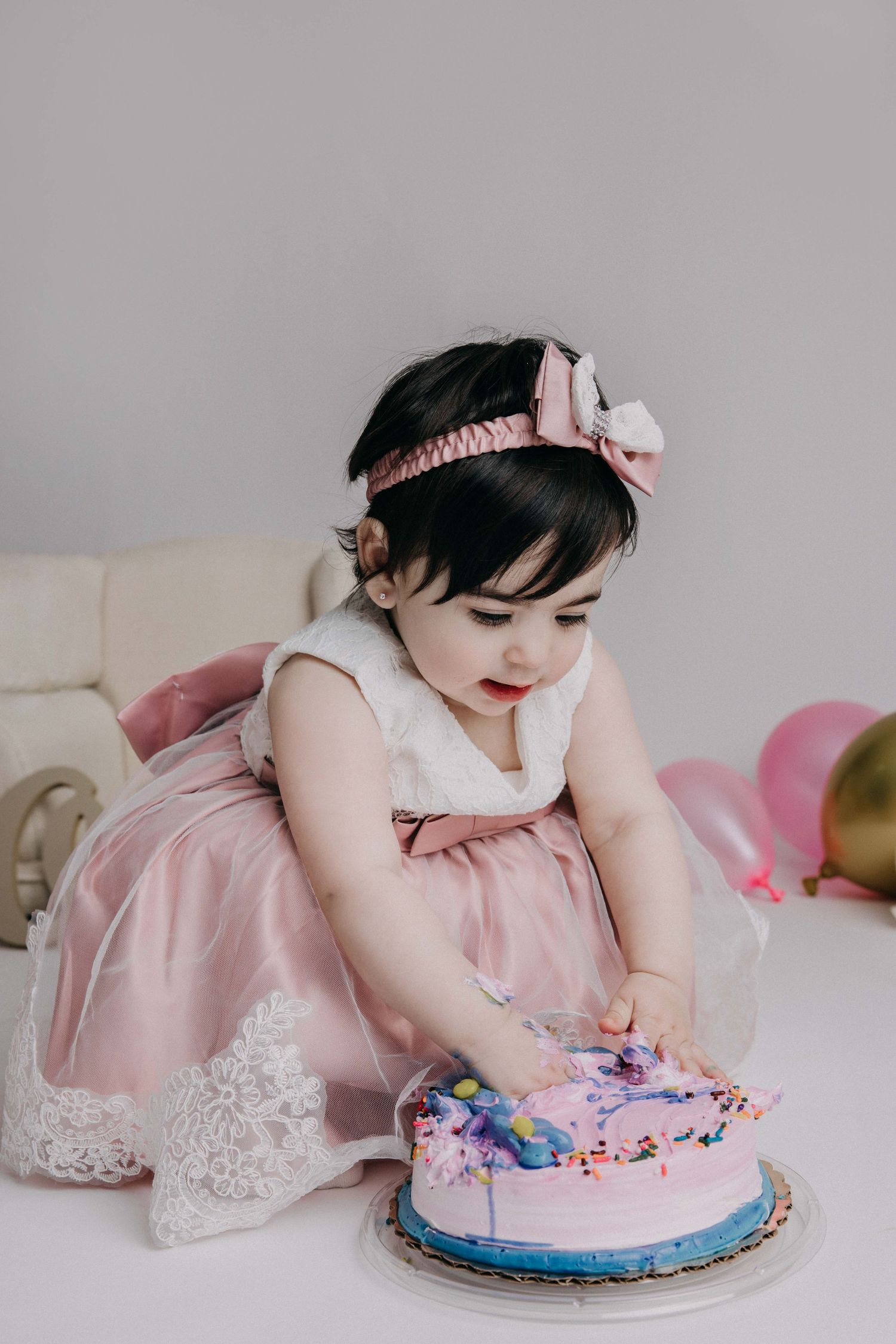 Child in pink dress celebrating with birthday cake in elegant party setting.