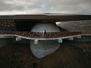 Modern architectural structure featuring curved metal surfaces and stone walls against a moody clouded sky.
