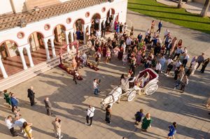 Aerial view of people walking through a grand outdoor plaza with ornate architectural features in golden sunlight.