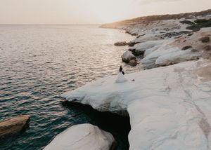 A person stands on white limestone cliffs overlooking the Mediterranean Sea at sunset, creating a dramatic coastal scene.