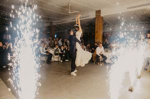 Dancing couple performs dramatic dip move at indoor wedding reception with sparkling cold spark effects on the dance floor.