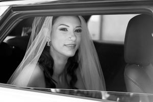 Bride in a white gown looks out the window of a car.
