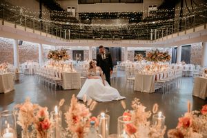 Elegant wedding reception venue decorated with hanging lights and coral floral centerpieces in a grand circular ballroom.