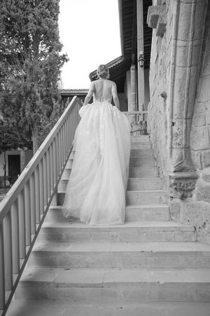 A black and white photograph of a bride in a flowing dress ascending stone steps at a historic building.