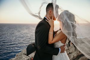 Couple embraces in romantic beachside wedding photo shoot during golden hour with flowing white veil.