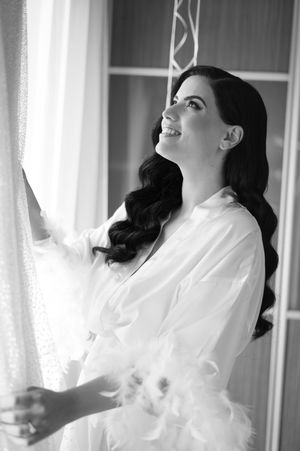 Black and white portrait of someone in a white robe looking up by a window.