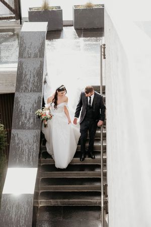 Wedding couple descending concrete stairs against white architectural backdrop.