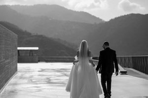 A wedding couple walks together on a rooftop terrace overlooking scenic mountain views in black and white.