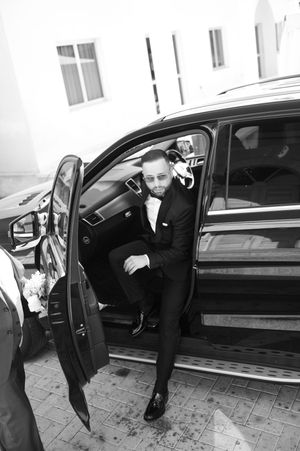 Person in formal black suit stepping out of luxury car in black and white photography.