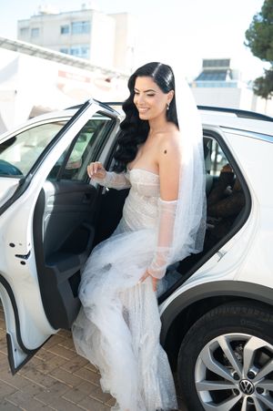 Elegant wedding dress being worn while entering a white car.